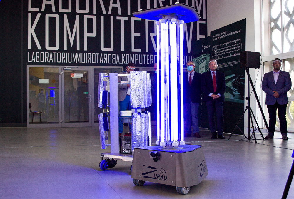 dwa świecące roboty, a w ich tle pięciu dorosłych mężczyzn