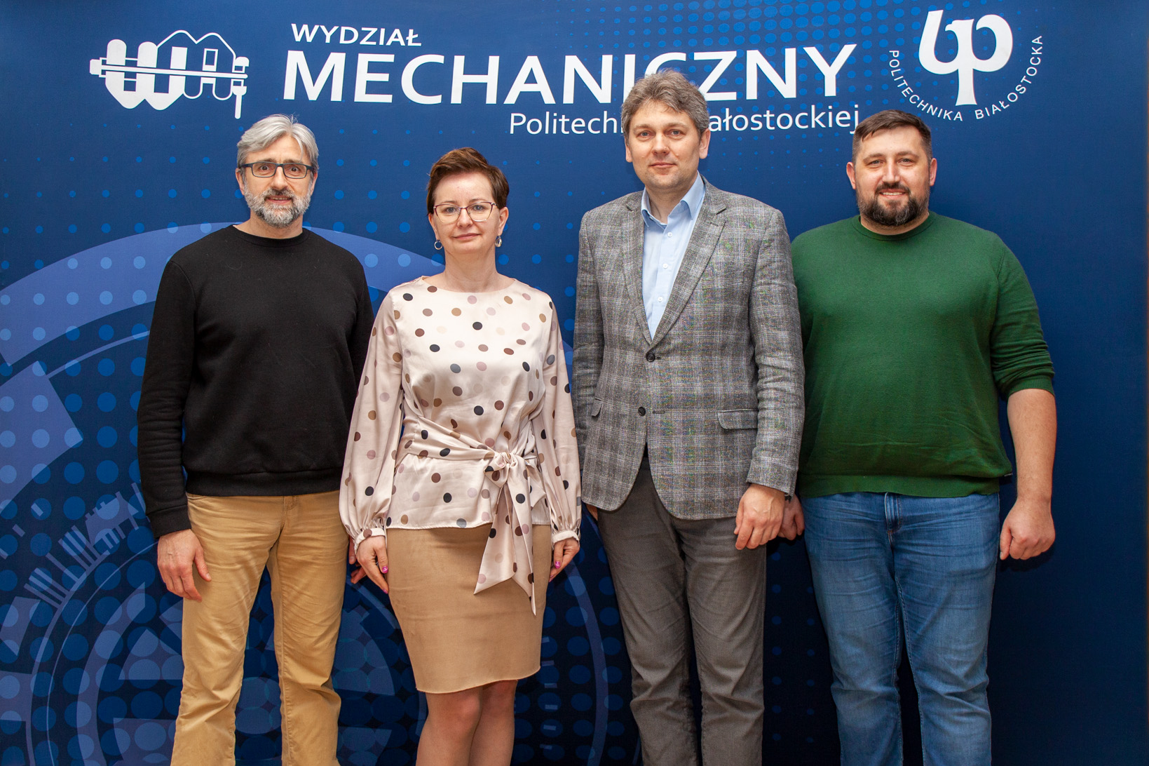 kobieta i trzech mężczyzn pozują na ściance reklamowej