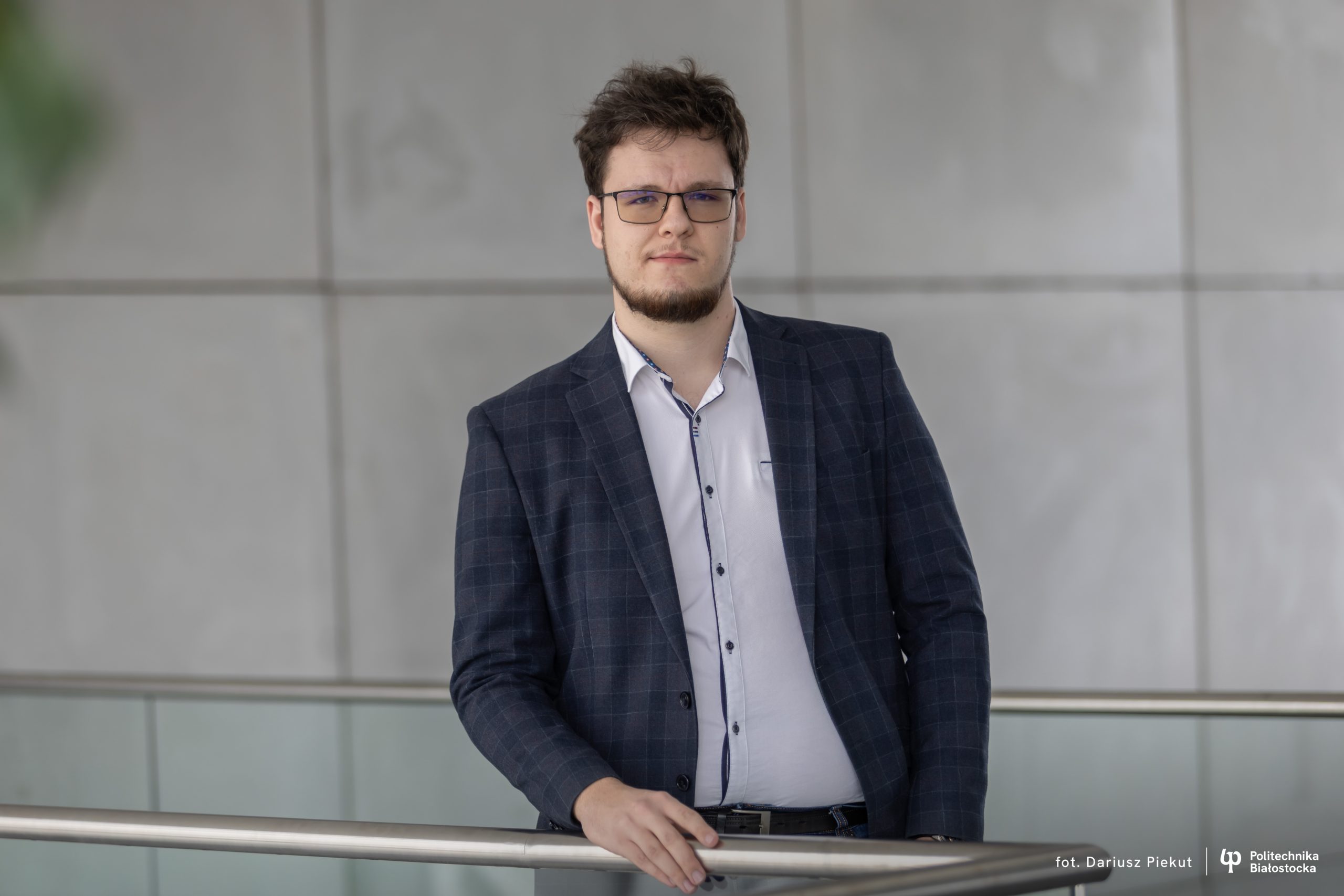 student pozuje na tle szarej ściany